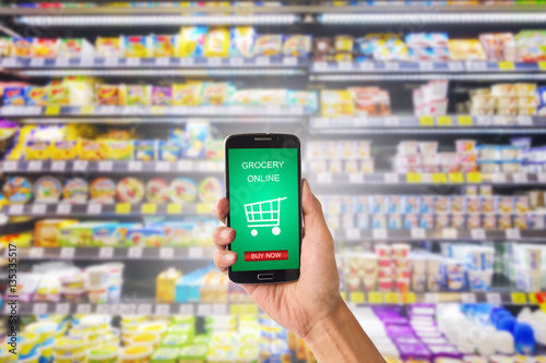 Hand holding mobile with grocery online on screen with blur supermarket background