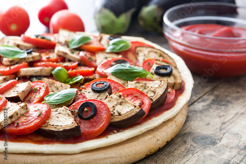 Vegetarian pizza with eggplant, tomato, black olives, oregano and basil on wooden background