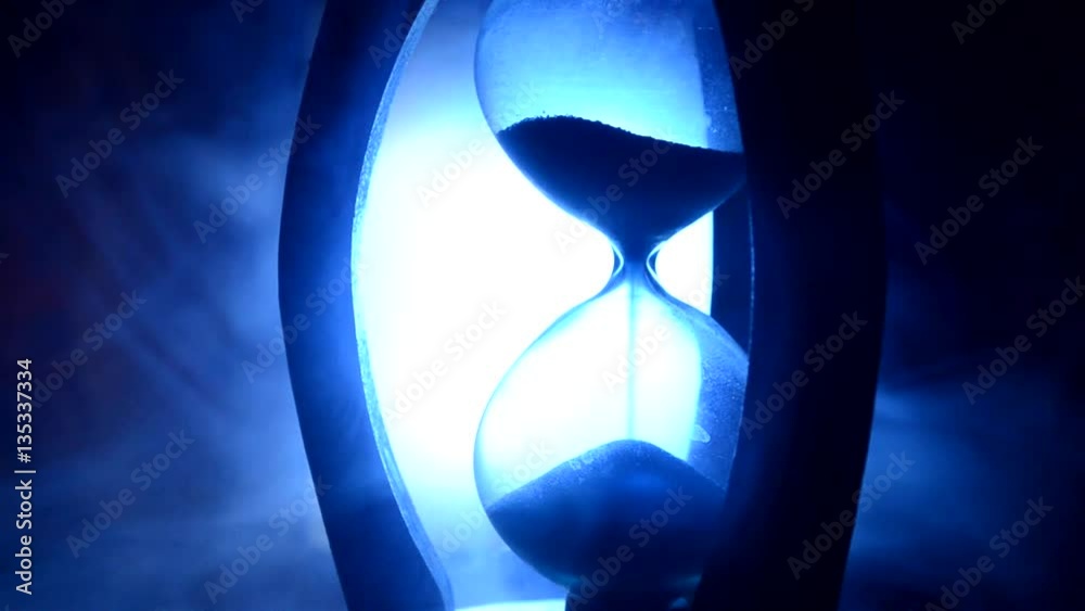 ime concept. Silhouette of Hourglass clock and old vintage wood clock with arrow and smoke on dark background with hot yellow orange blue cold back lighting, or symbols of time under smoke, the end
