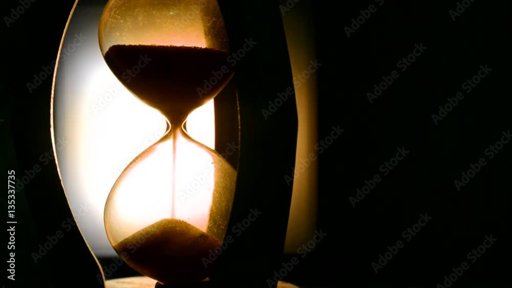 ime concept. Silhouette of Hourglass clock and old vintage wood clock with arrow and smoke on dark background with hot yellow orange blue cold back lighting, or symbols of time under smoke, the end