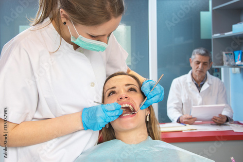 Young woman on medical exam at dentist office. Dentist in the background.