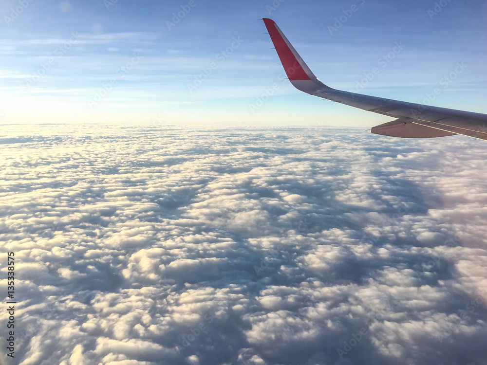 Wing of airplane flying above the clouds in the sky Wing of airplane flying above the clouds in the sky