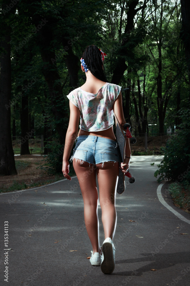 Stylish and sexy girl in erotic shorts walking in the park with a  skateboard in hands Stock 写真 | Adobe Stock