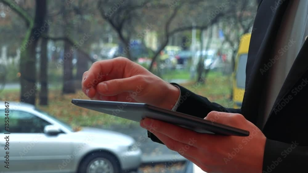 A man works on a tablet - closeup on the hands, a street in the background A man works on a tablet - closeup on the hands, a street in the background