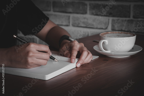 Close up of people hand writing on notebook on wooden table