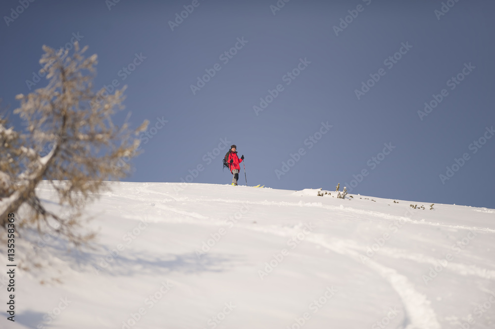 Man standing on top of the hill and preparing to go skiing down a piste. It is beautiful sunny day with blue sky.