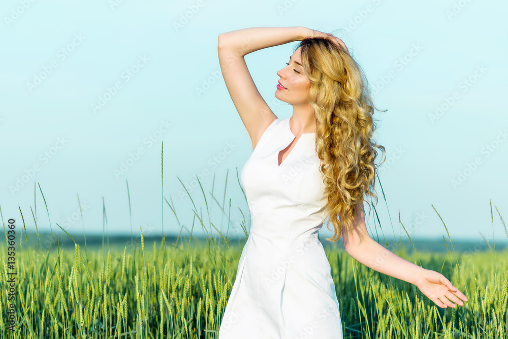 Young Girl in a field of wheat enjoying sunny day nature. Springtime green field growing harvest