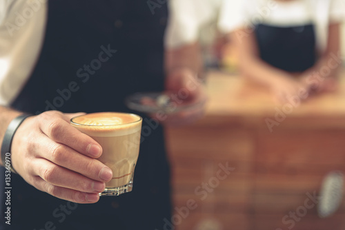 Waiter holding glass of tasty latte with tulip art
