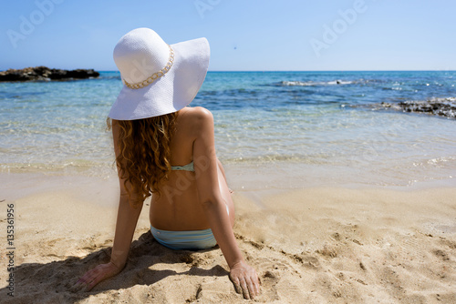 Young woman sitting on the beach. Portrait of a girl in white hat relaxing at...