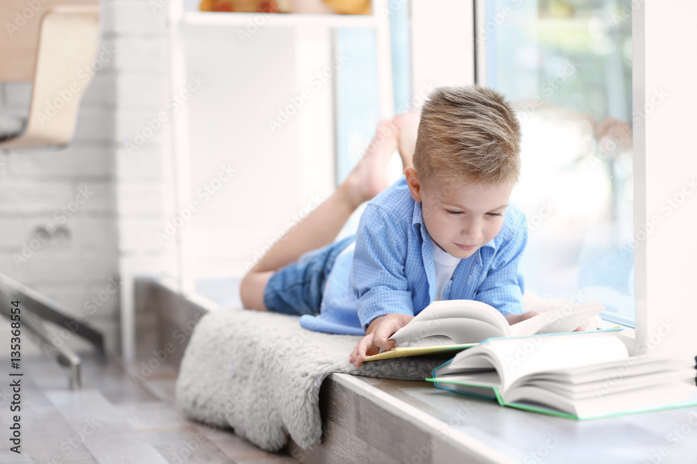 Cute boy reading interesting book on windowsill Cute boy reading interesting book on windowsill