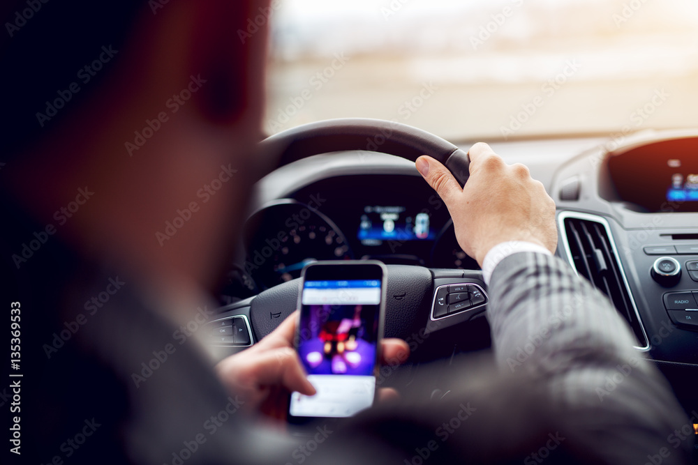 Man looking at mobile phone while driving a car.