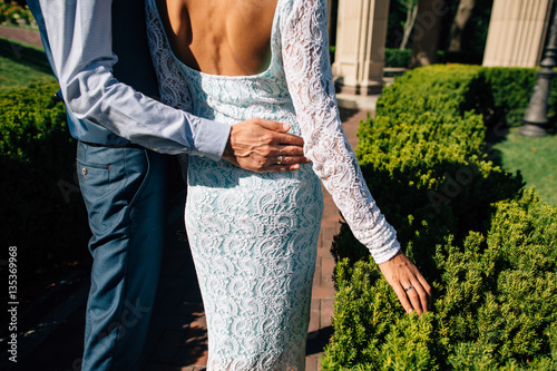 Back of bride. Groom hugs bride's waist on their wedding day photo