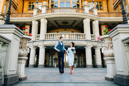 Happy newlyweds running on the background of luxury mansion on wedding day