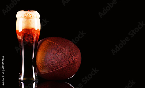 Beer glass with foam and American football ball on black background