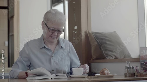 A pensioner with a stylish haircut and glasses spending time in cafes, reading an interesting book and drinking tea. Reading the book: old beautiful woman with a book.