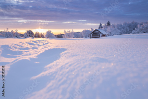 Golden sunlight over an idyllic white winter landscape with a little wooden hut in background