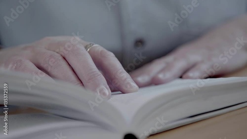 Close-up of reading a book and flipping pages. Hands of a mature and middle-aged woman holding a book and turning the pages. Leisure and hobbies in retirement.