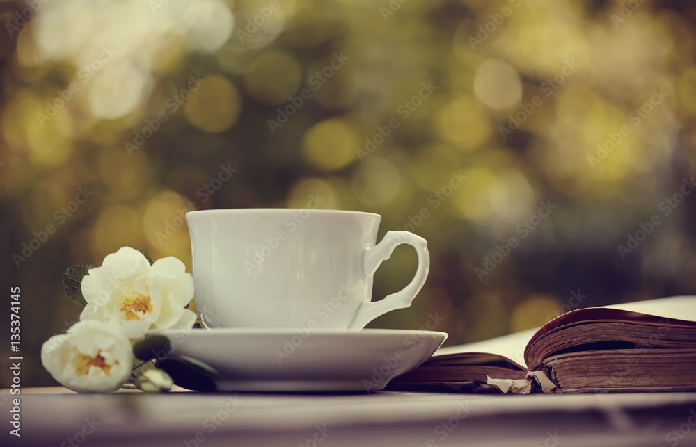 Old open book and a white cup with a wild roses Old open book and a white cup with a wild roses