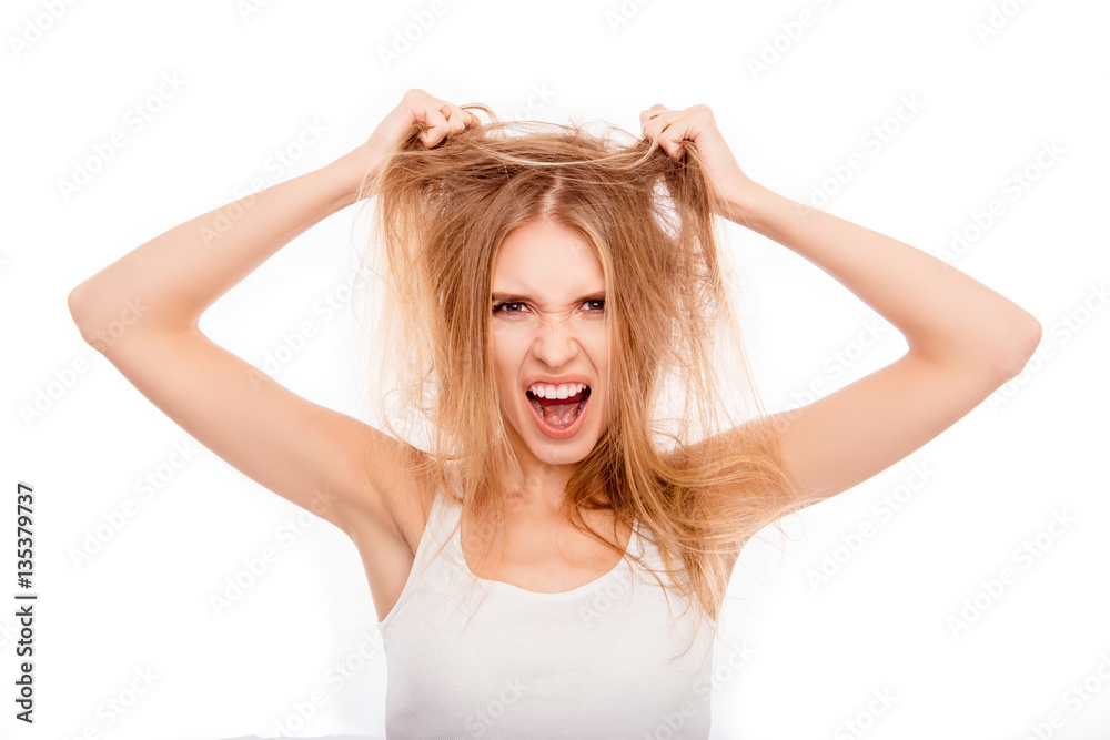 Frustrated young blonde holding her damaged hair and yelling