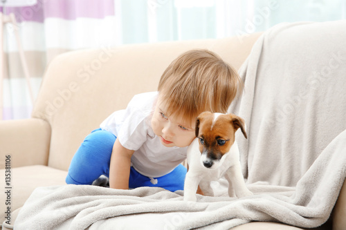 Cute little boy with puppy on sofa at home