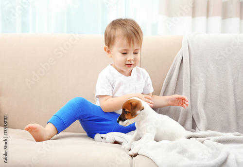 Cute little boy with puppy on sofa at home © Africa Studio