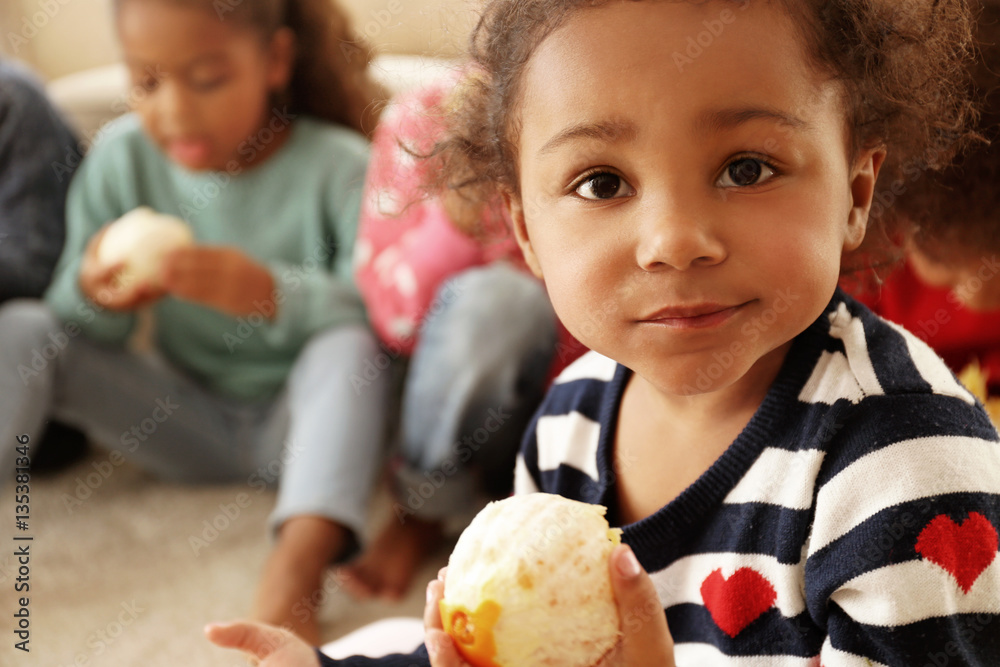 Fototapeta premium Cute African girls sitting on floor and eating orange