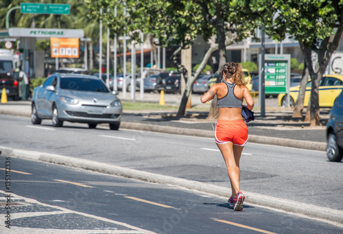 The woman jogging on the beachfront running path in front of the traffic road with cars next to the petrol station at Copacabana Beach, Rio de Janeiro, Brazil