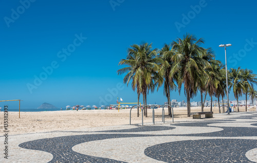Fototapeta Naklejka Na Ścianę i Meble -  Copacabana beach with white sand, blue sky, green palms and mosaic floor, black and white Portuguese pavement in Rio de Janeiro, Brazil