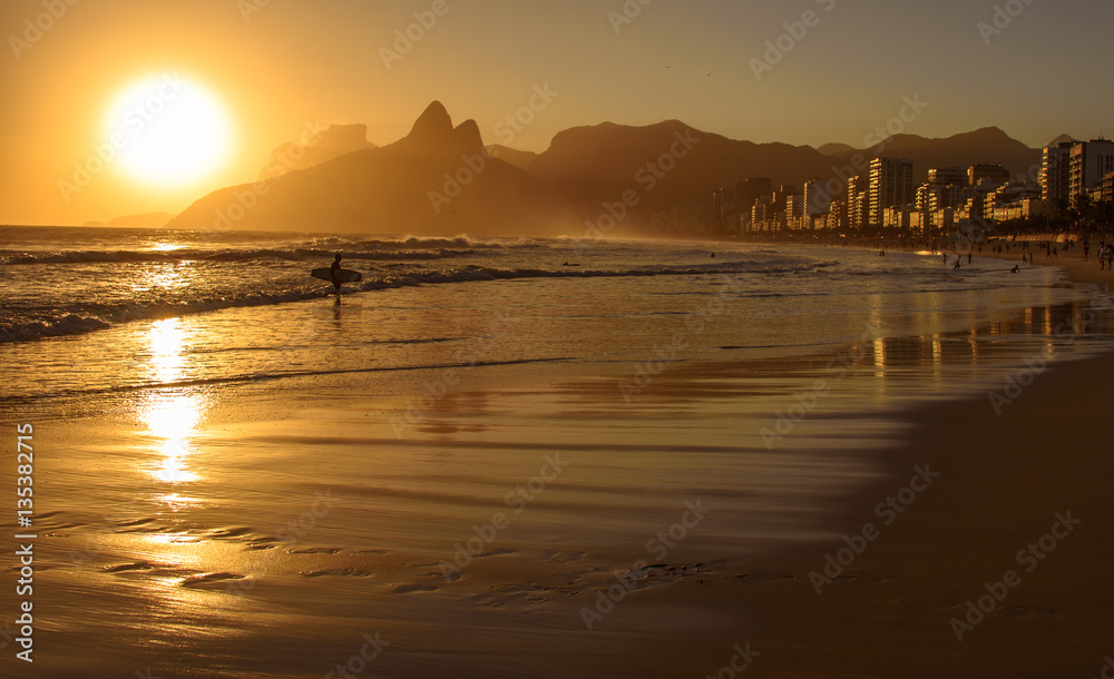 Fototapeta premium Golden sunset with Two Brothers Dois Irmaos Mountain and surfer silhouette at Ipanema Beach, Rio de Janeiro, Brazil