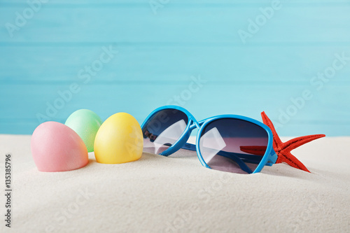 Easter eggs with sand and sunglasses, on wooden blue background