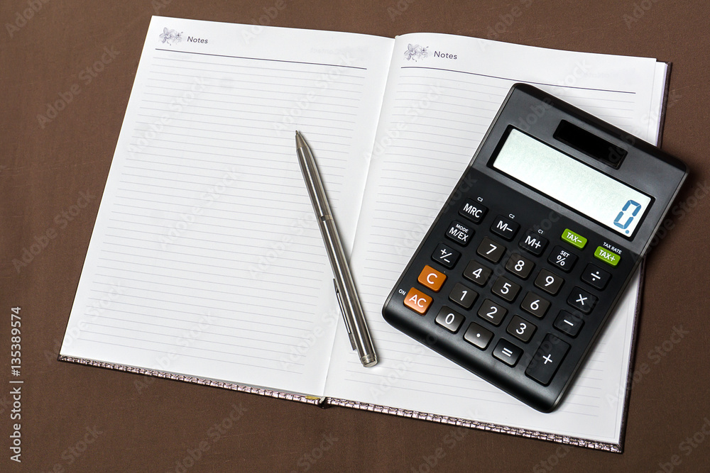 Notebook, calculator and silver pen on brown cloth background. Notebook, calculator and silver pen on brown cloth background.