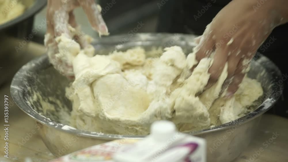 Closeup hands of cooker kneads dough in bowl industrial kitchen setting. chef blue apron with strong arms in sticky mixture kneading pastry in iron dish indoors. Preparing for restaurant menu bakery Closeup hands of cooker kneads dough in bowl industrial kitchen setting. chef blue apron with strong arms in sticky mixture kneading pastry in iron dish indoors. Preparing for restaurant menu bakery
