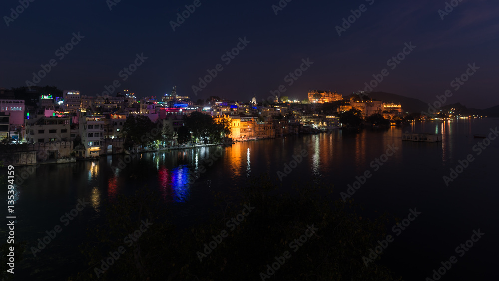 Glowing cityscape at Udaipur by night. The majestic city palace reflecting lights on Lake Pichola, travel destination in Rajasthan, India