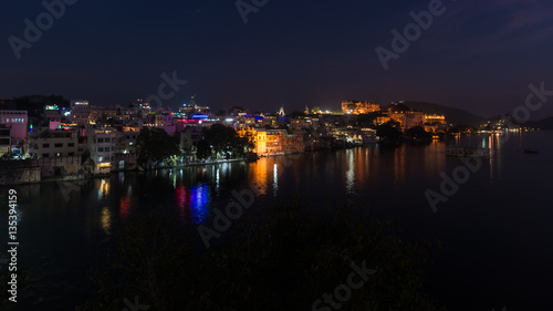 Glowing cityscape at Udaipur by night. The majestic city palace reflecting lights on Lake Pichola, travel destination in Rajasthan, India