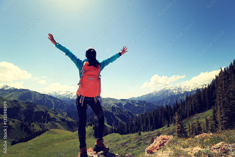cheering young woman backpacker hiking on forest mountain peak