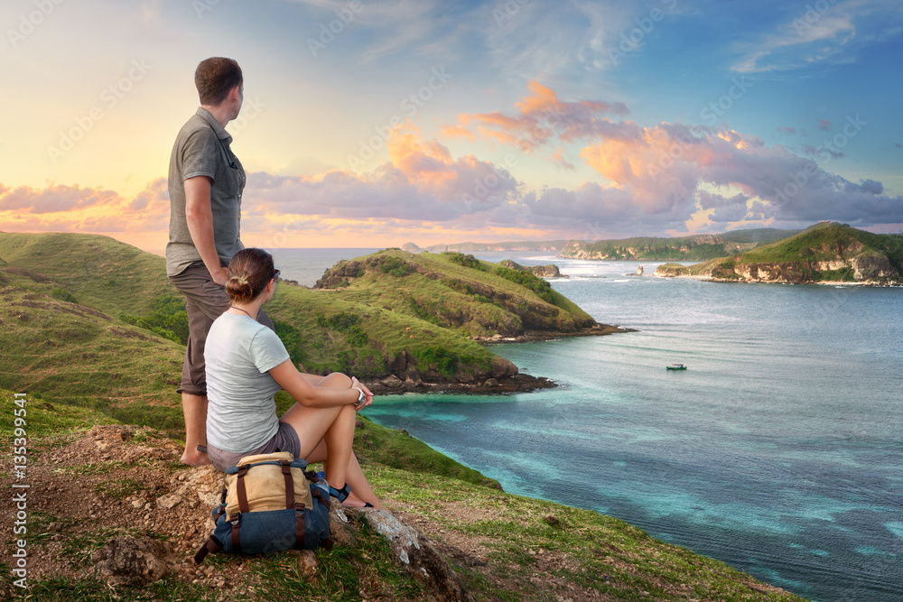 Couple hikers with backpacks enjoying sunset at mountain coast Couple hikers with backpacks enjoying sunset at mountain coast