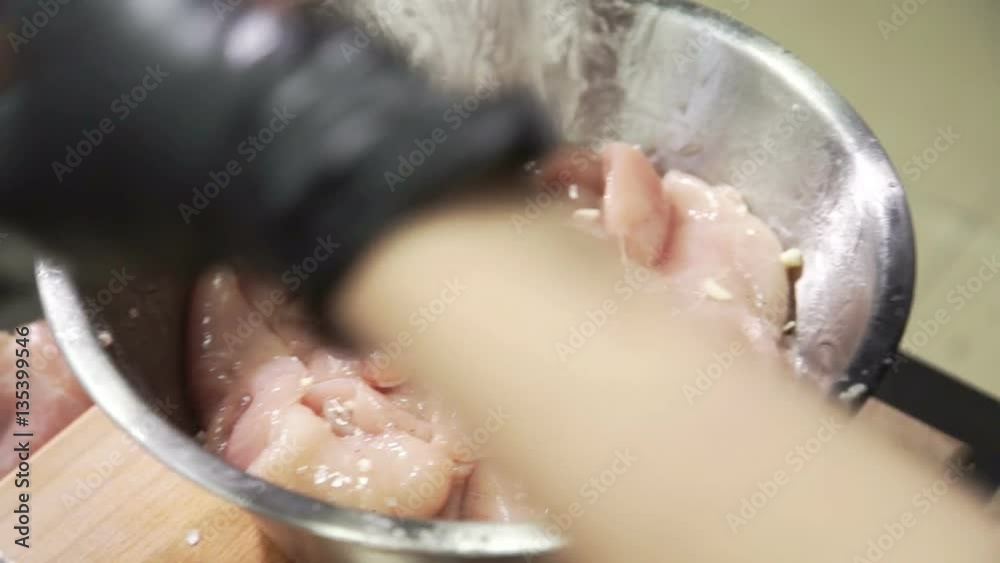 harvesting food marinade for chicken in a restaurant indoors shifted in metal containers for temporary storage. Close up shooting of hands in black rubber gloves for wet products mixing pieces of meat