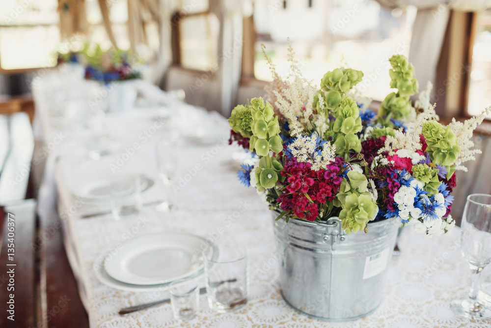 Bucket with bouquet of red, white and blue flowers stands on whi Bucket with bouquet of red, white and blue flowers stands on whi