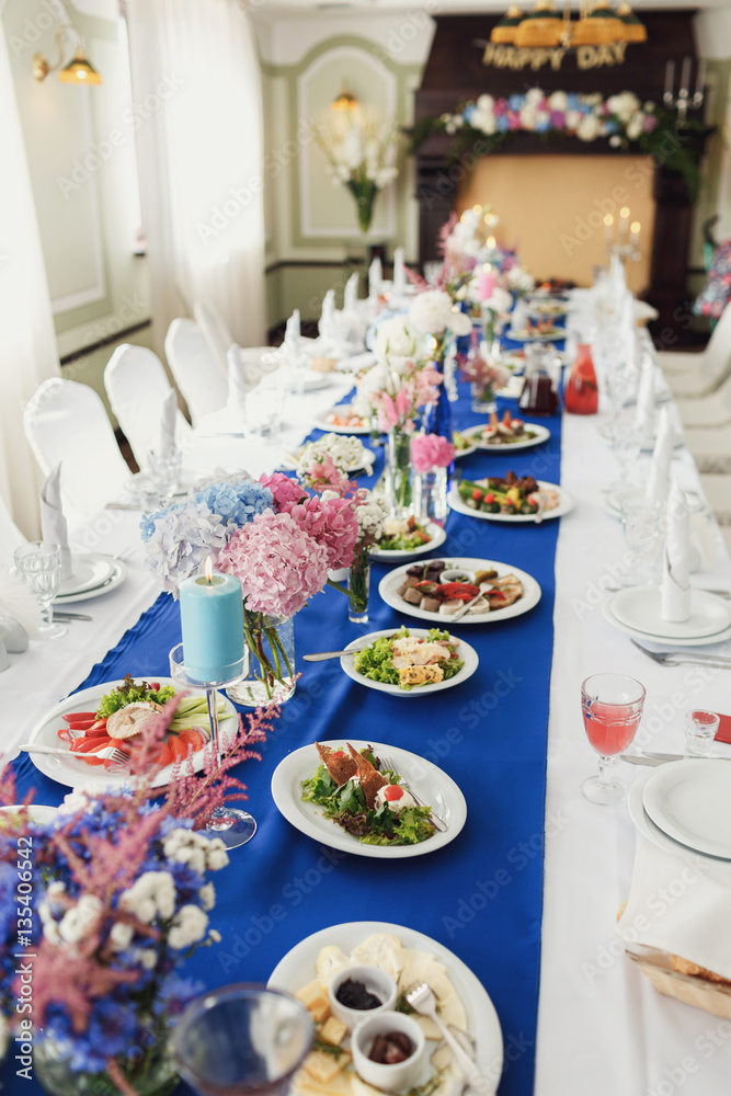 Plates with salads and vases with flowers stand on blue cloth