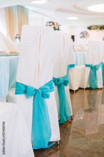 White chairs decorated with blue ribbons stand around dinner tab