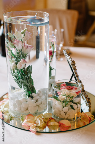 Glass vases with roses in water and little candles on top stand