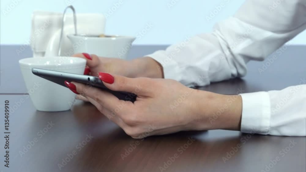 Female hands using tablet and holding coffee cup Female hands using tablet and holding coffee cup