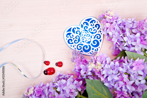 Fototapeta Naklejka Na Ścianę i Meble -  Lilac flowers and blue ornamental openwork heart on a wooden background. Card