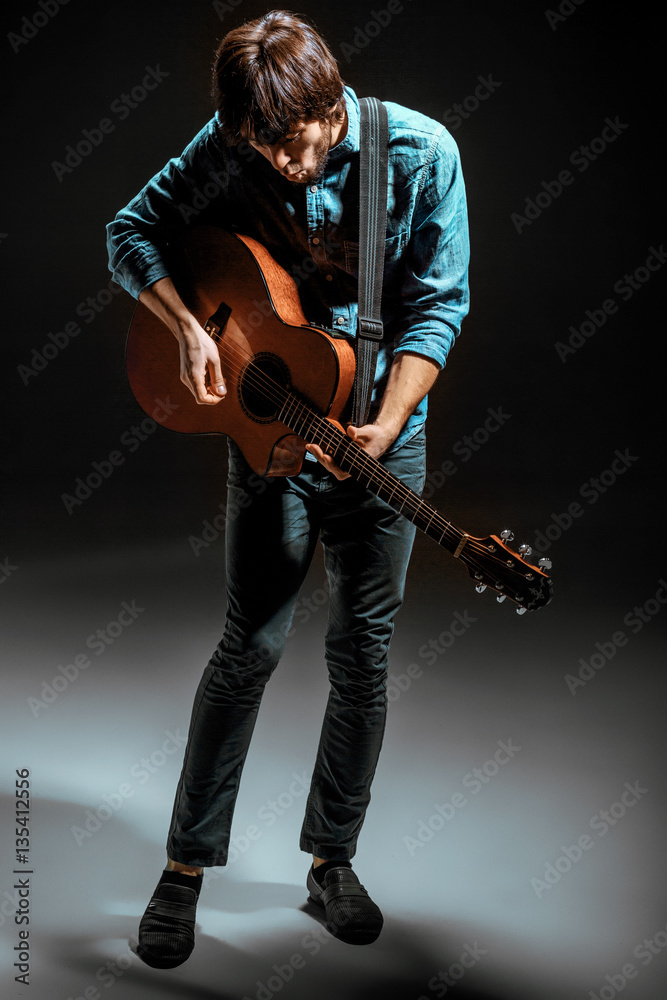 Cool guy standing with guitar on dark background