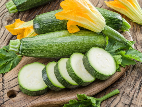 Zucchini with slices and zucchini flowers on a wooden table.