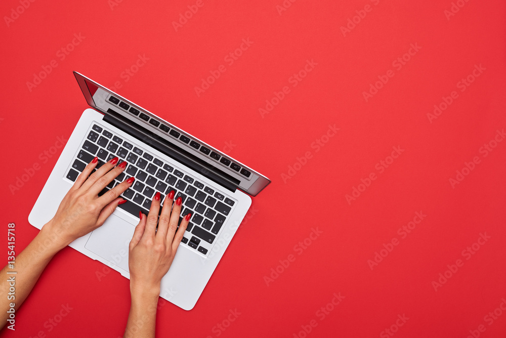 Woman skinny hands working on a silver laptop on a red desktop a - obrazy, fototapety, plakaty 