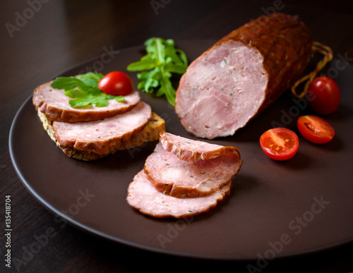 Smoked sausage, ham with red tomatoes and herbs on a dark plate