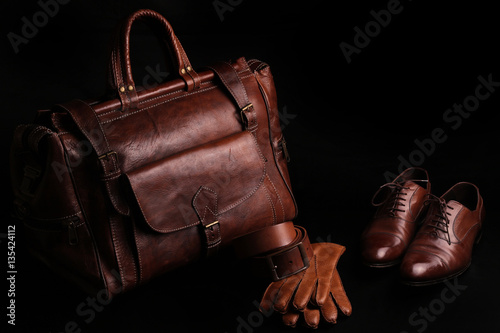 Luxury leather brown men's accessories, travel bag, belt, gloves, shoes. isolated on black background