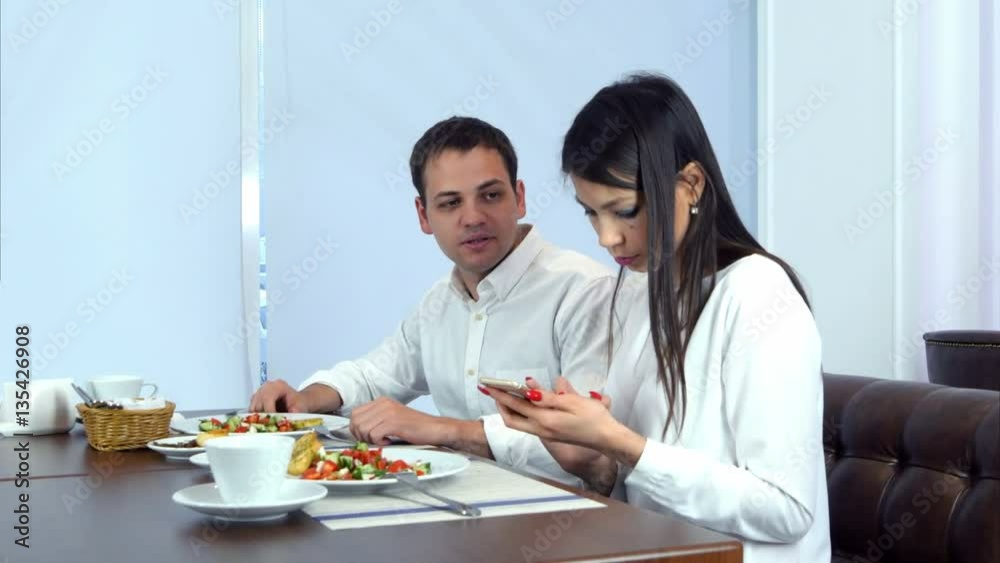 Young man paying the bill while his girlfriend checking her phone Young man paying the bill while his girlfriend checking her phone