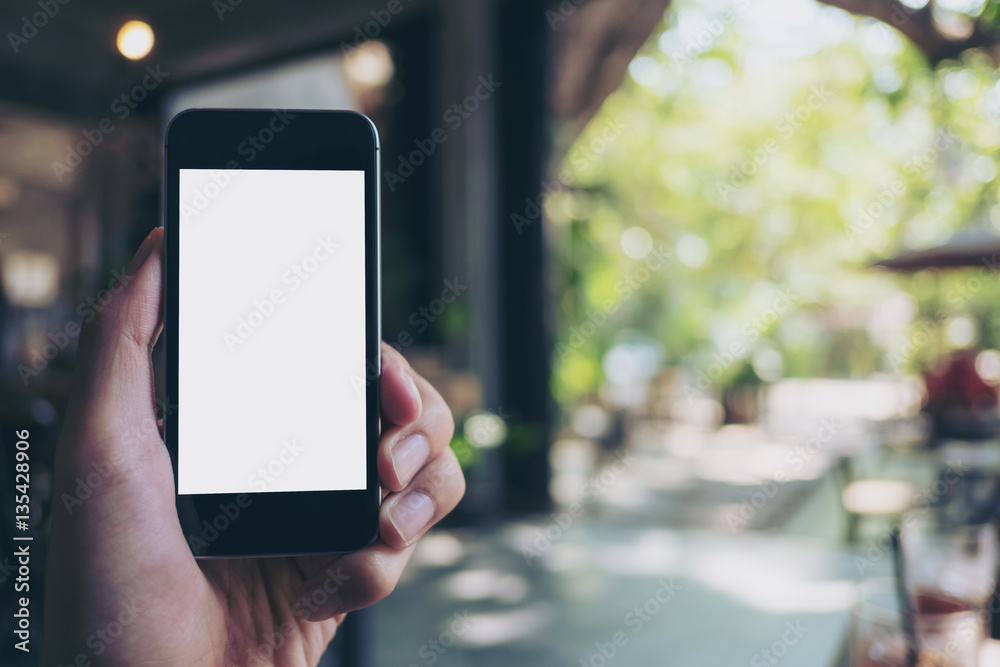 Mockup image of hand holding black mobile phone with blank white screen in loft cafe and green nature